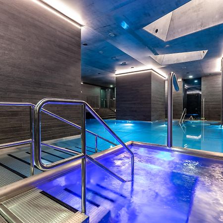 Grandhotel Pupp Karlovy Vary Ngoại thất bức ảnh The photo shows a modern spa area with a pool. There are sleek, dark walls and blue lighting that creates a tranquil atmosphere. A metal railing leads down into the pool, which has a section with bubbling water. The overall design features clean line