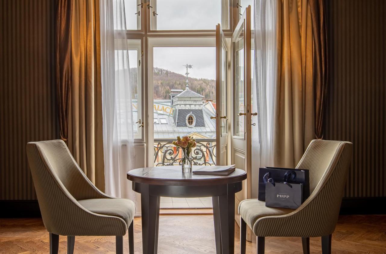 Grandhotel Pupp Karlovy Vary Ngoại thất bức ảnh The photo depicts a cozy interior setting, likely within a hotel room or a private space. There are two elegant chairs positioned around a round wooden table. On the table, there is a small vase with flowers, adding a touch of warmth to the environme