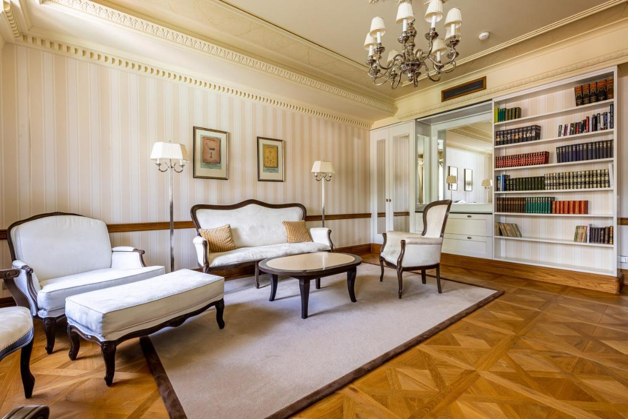Grandhotel Pupp Karlovy Vary Ngoại thất bức ảnh The photo shows a spacious and elegantly designed living room. It features a light color palette with subtle striped wallpaper. In the center, there is a round coffee table surrounded by two armchairs and a modest sofa, all in a classic style. A chan