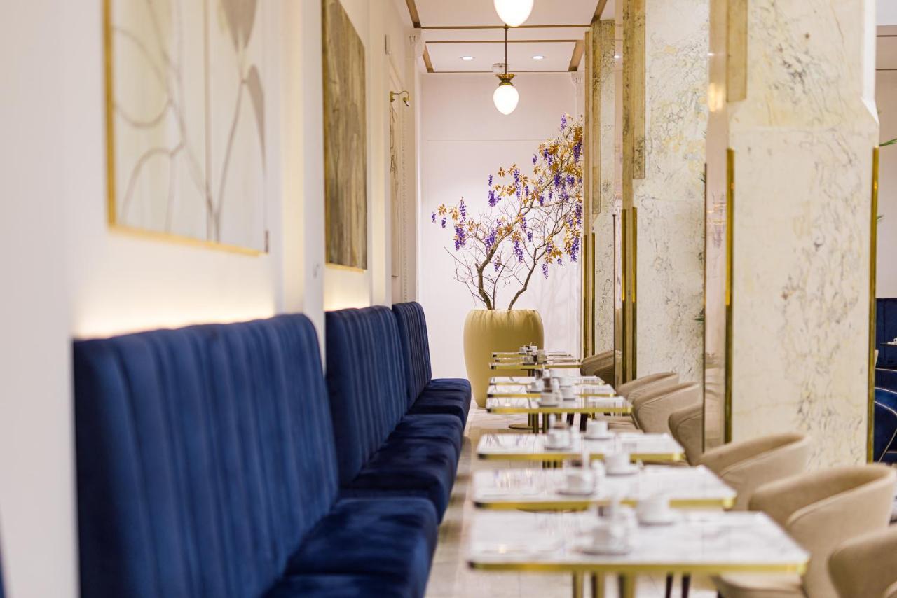 Grandhotel Pupp Karlovy Vary Ngoại thất bức ảnh The photo shows a stylish and elegant interior of a café or restaurant. On one side, there are long, plush blue benches against the walls, providing seating for guests. The tables are set with white plates and cutlery, suggesting a careful arrangemen