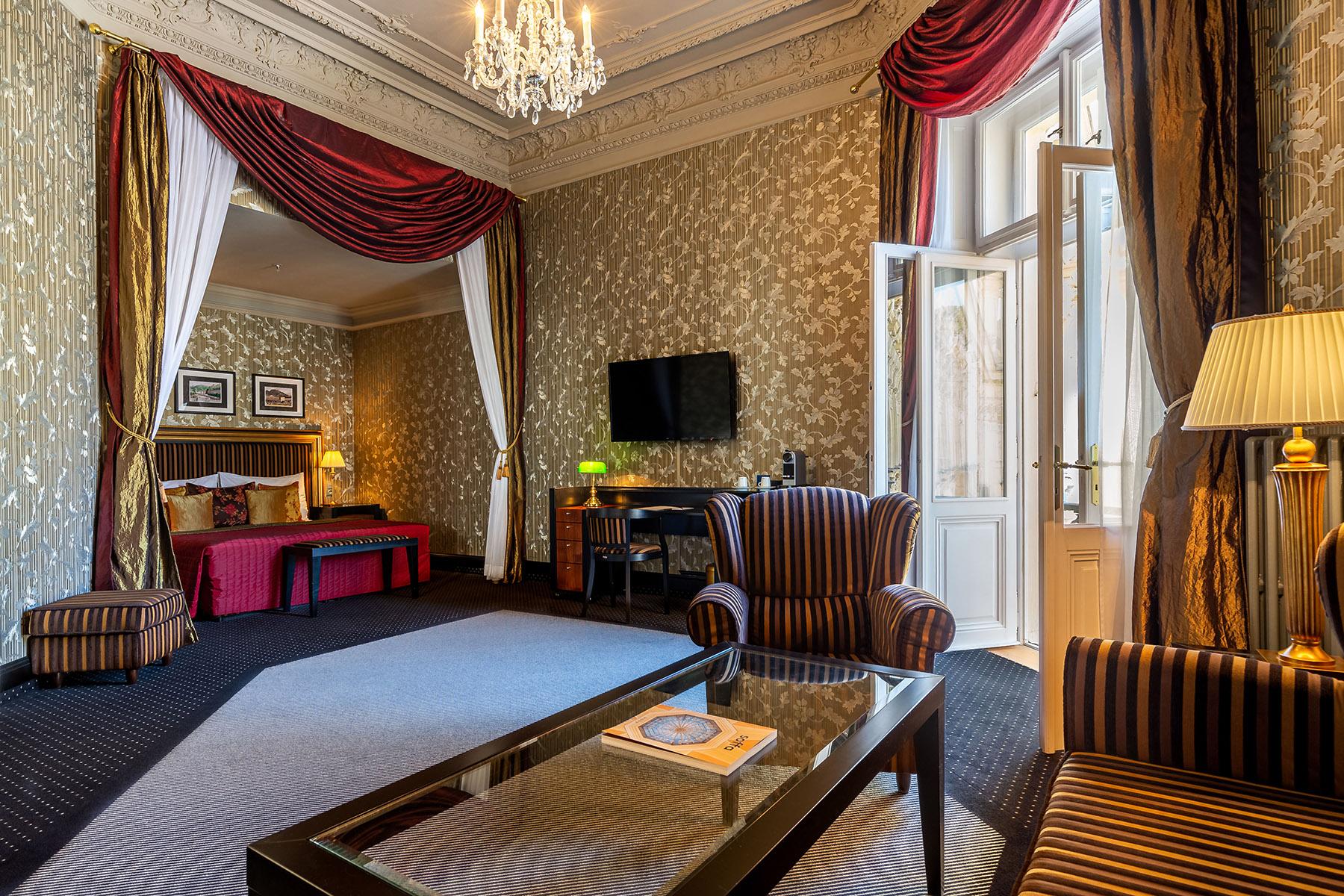 Grandhotel Pupp Karlovy Vary Ngoại thất bức ảnh The photo shows a luxurious hotel room featuring elegant decor. The room has tall windows with flowing curtains, a plush carpet, and ornate wallpaper. There are two comfortable armchairs with a stylish design positioned around a glass coffee table. A