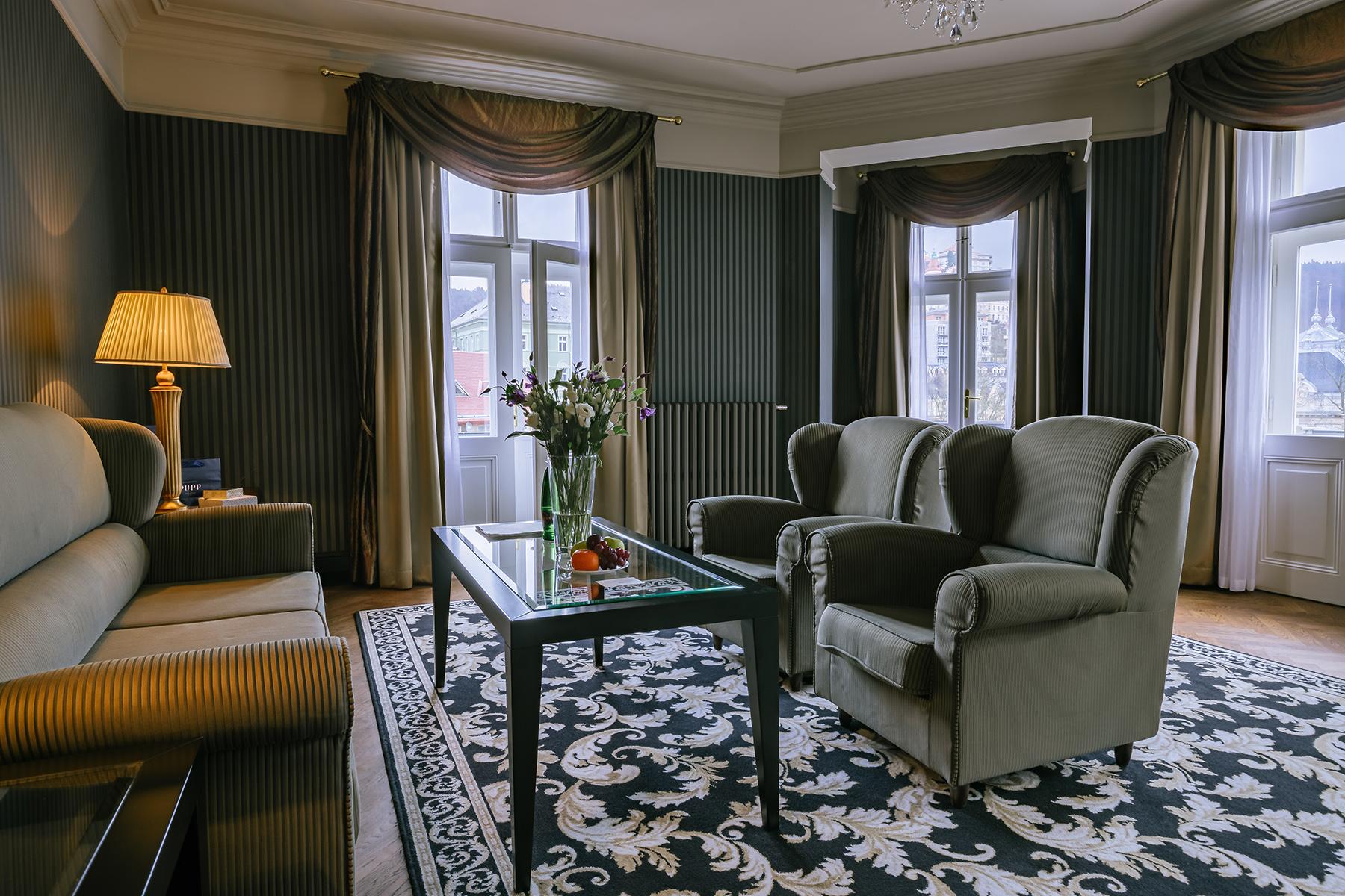 Grandhotel Pupp Karlovy Vary Ngoại thất bức ảnh The photo shows a cozy living room with a warm and elegant decor. It features two green upholstered armchairs and a beige sofa. In the center, there’s a glass coffee table with a small vase of flowers. The room is enhanced by dark wallpaper and soft 
