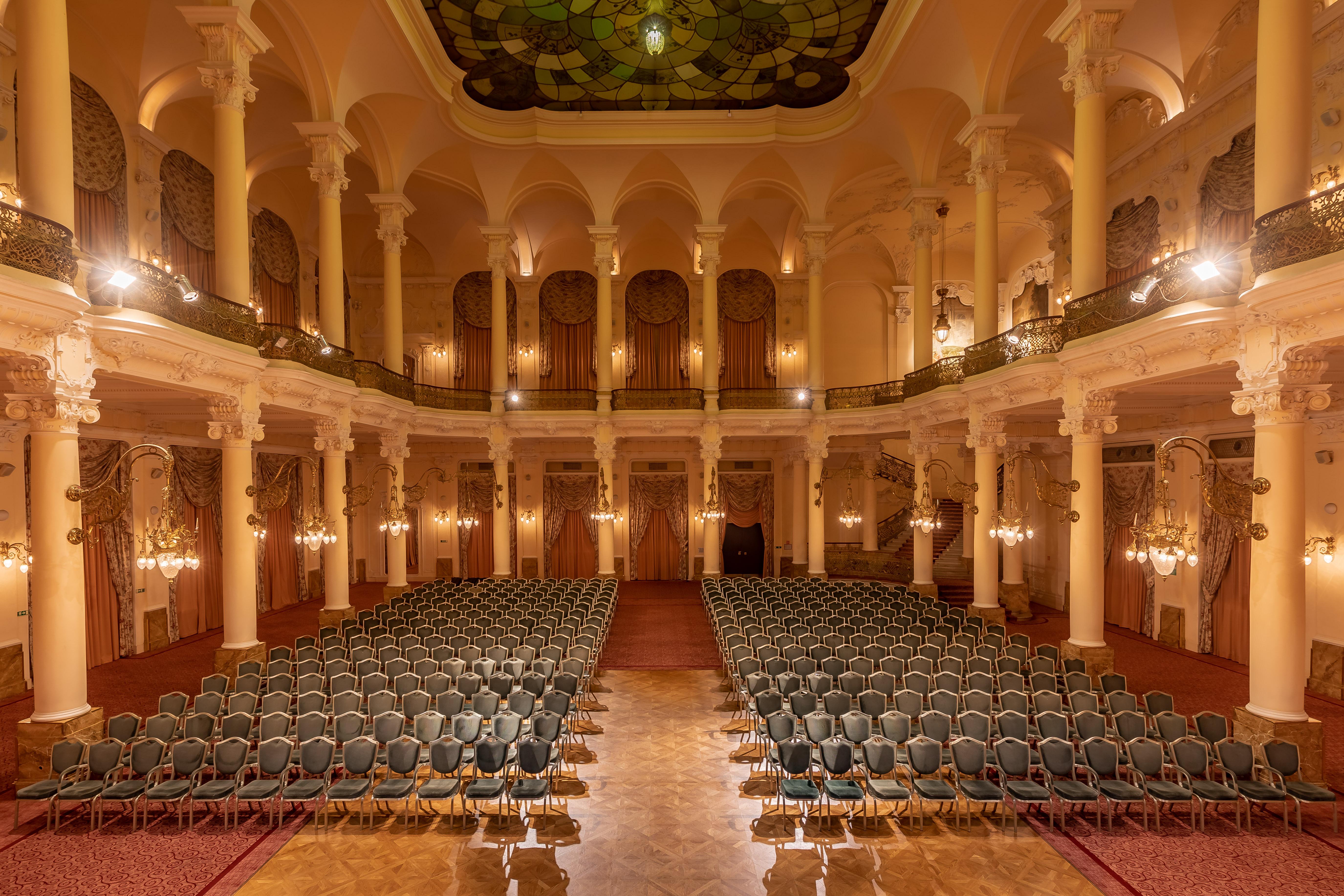Grandhotel Pupp Karlovy Vary Ngoại thất bức ảnh The photo shows an elegant, spacious auditorium or hall, designed for events or performances. The interior features high ceilings supported by tall, decorative columns. Rows of green upholstered chairs are neatly arranged, suggesting the space is set