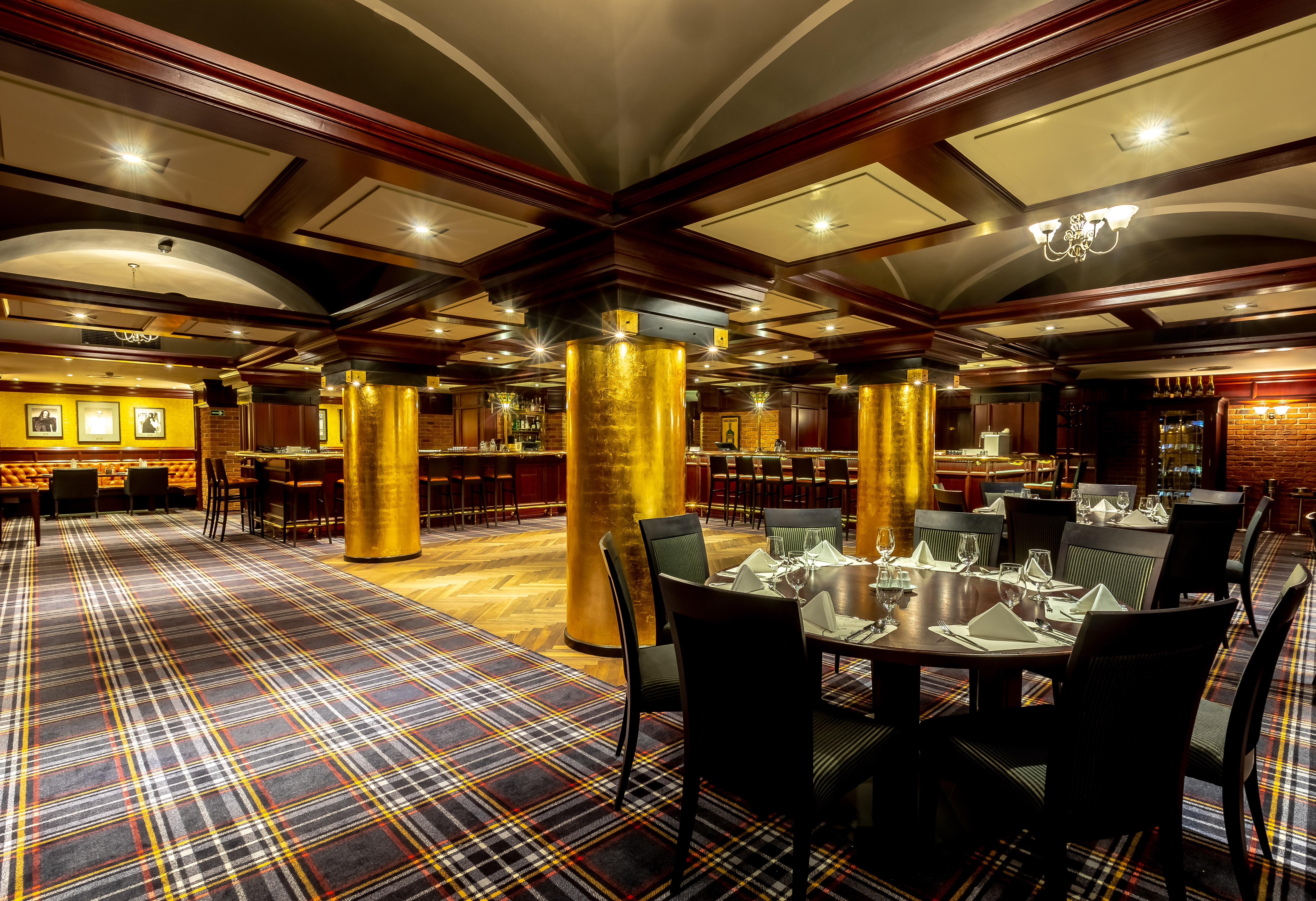 Grandhotel Pupp Karlovy Vary Ngoại thất bức ảnh The photo shows an elegant dining area in a restaurant. The interior features a modern design with a checkered carpet and wooden accents. Golden columns are prominent in the space, adding a touch of luxury. The tables are set with neat tableware, and