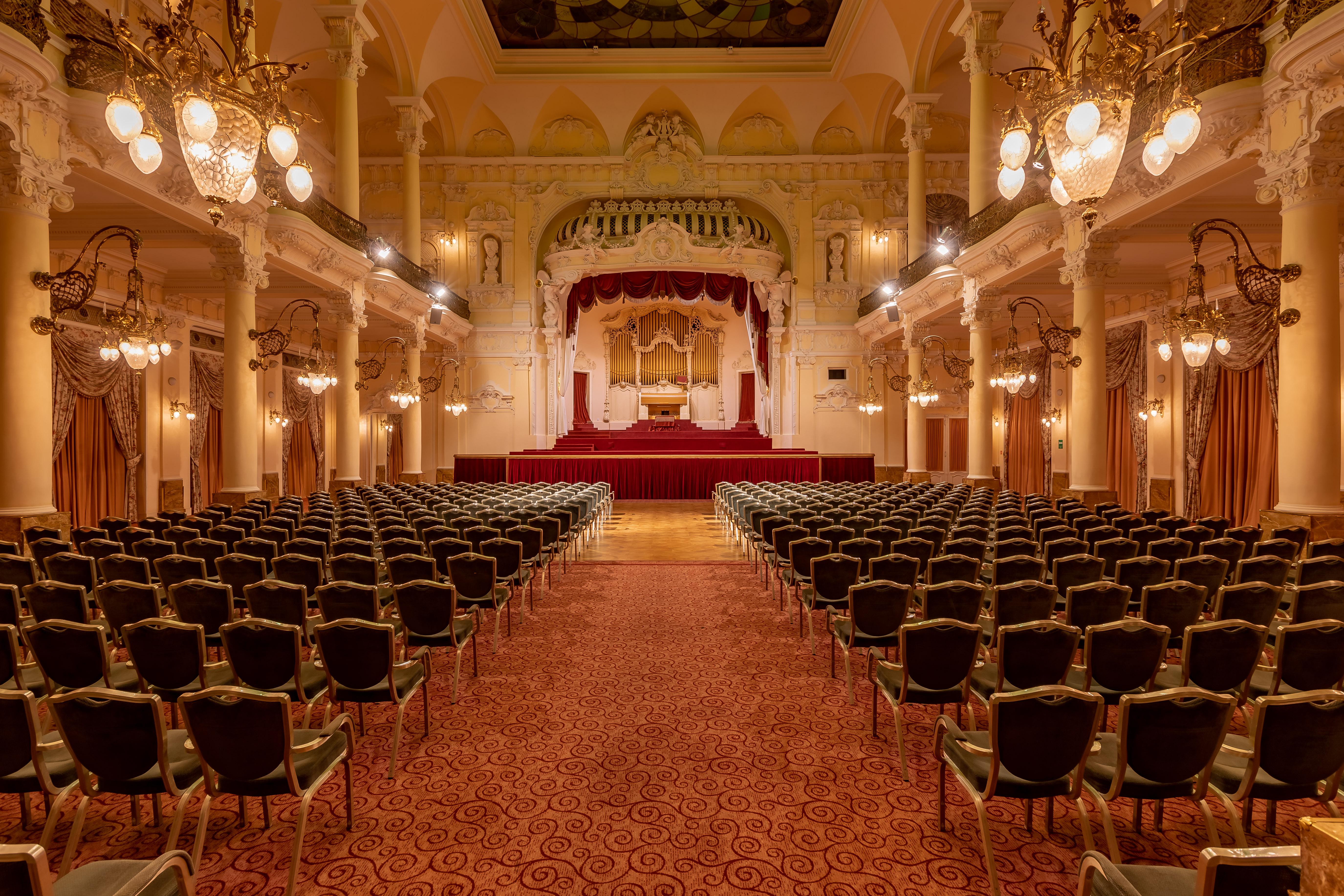 Grandhotel Pupp Karlovy Vary Ngoại thất bức ảnh The photo showcases an elegant interior of a theater or concert hall. It features a grand stage in the background, adorned with red curtains and decorative elements. The seating area is filled with rows of green upholstered chairs arranged in a symme