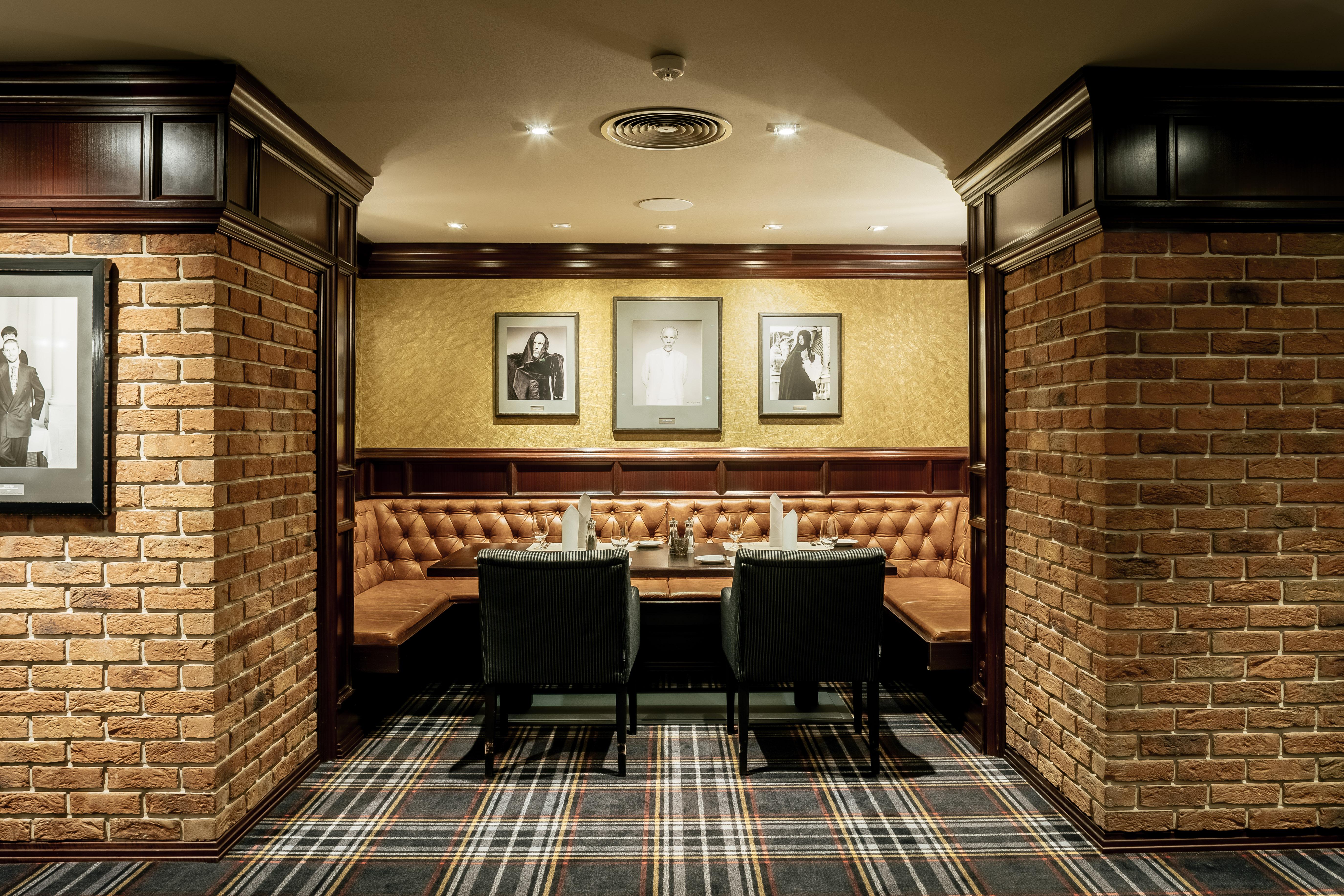 Grandhotel Pupp Karlovy Vary Ngoại thất bức ảnh The photo depicts a cozy interior of a room, likely a restaurant or lounge. It features brick walls, giving it a rustic feel, and wooden paneling adds a touch of elegance. There are two black chairs positioned at a wooden table. The seating area is c