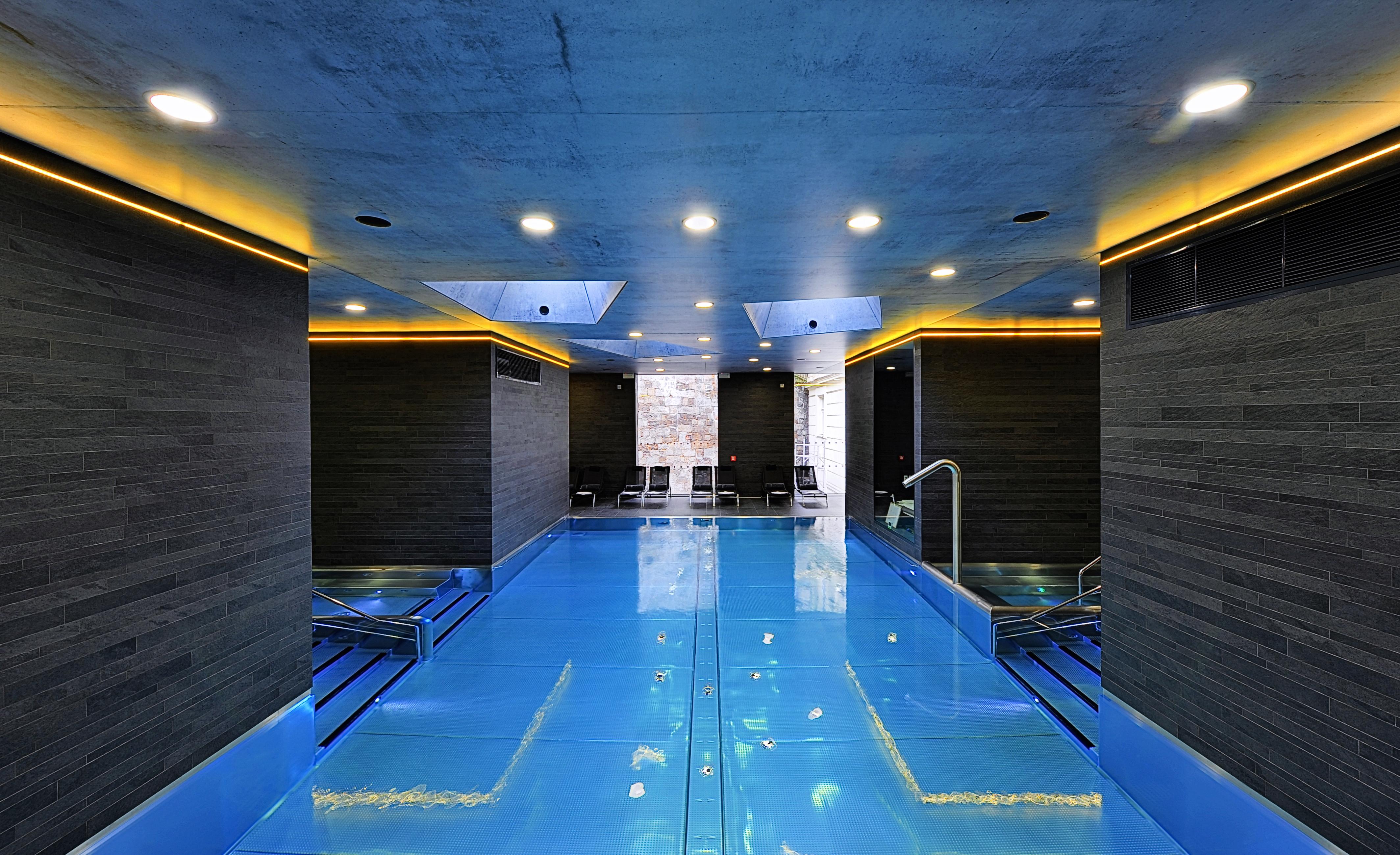 Grandhotel Pupp Karlovy Vary Ngoại thất bức ảnh The photo shows a modern indoor swimming pool area. The pool features a striking blue surface and is surrounded by sleek, dark walls. Ambient lighting, including soft yellow or warm lights along the edges, enhances the contemporary aesthetic. There a