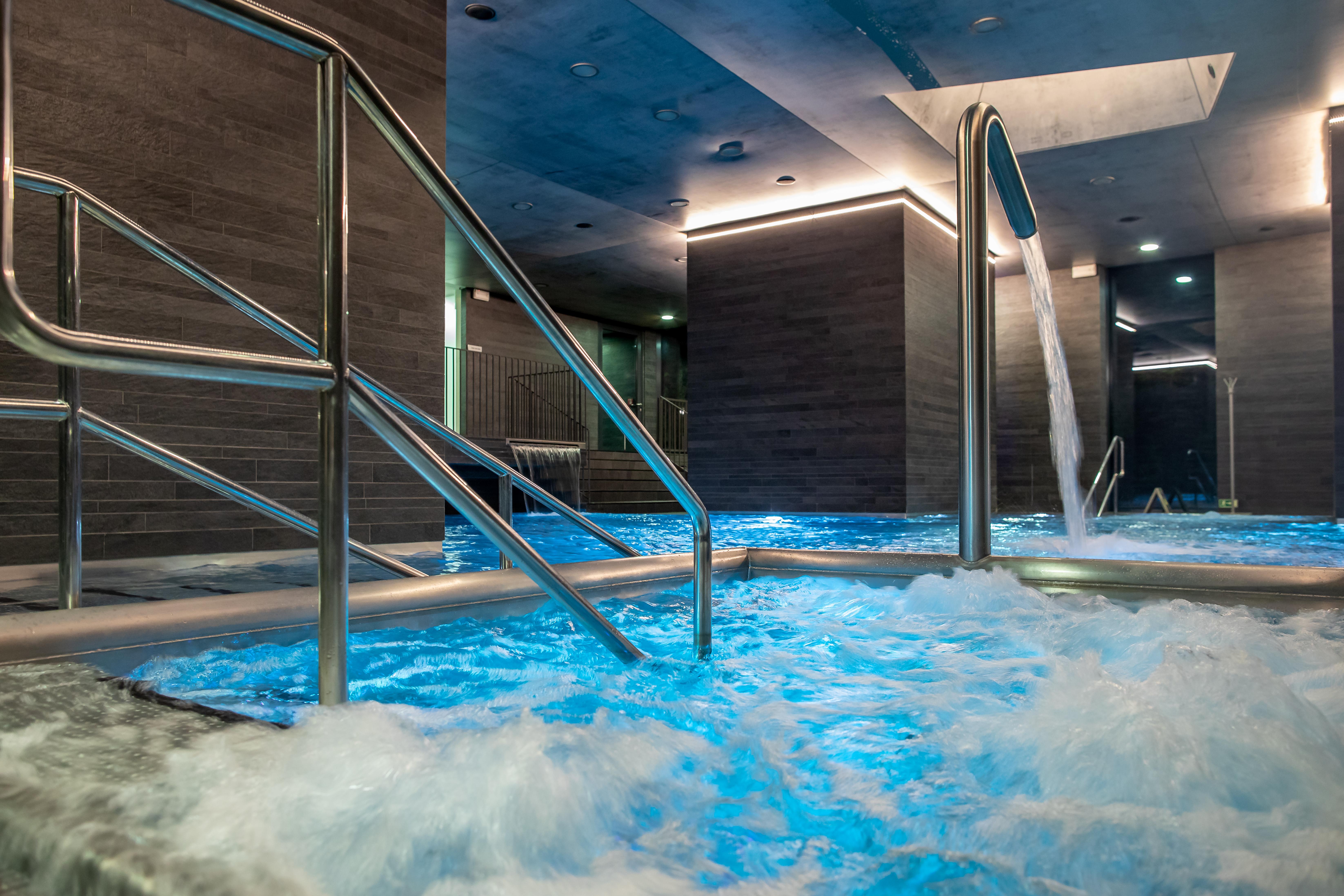 Grandhotel Pupp Karlovy Vary Ngoại thất bức ảnh The photo shows a sleek, modern spa area featuring a hot tub or pool with bubbling, illuminated blue water. There are stainless steel handrails leading into the water. The walls have a contemporary design with a gray finish, and there are soft lights