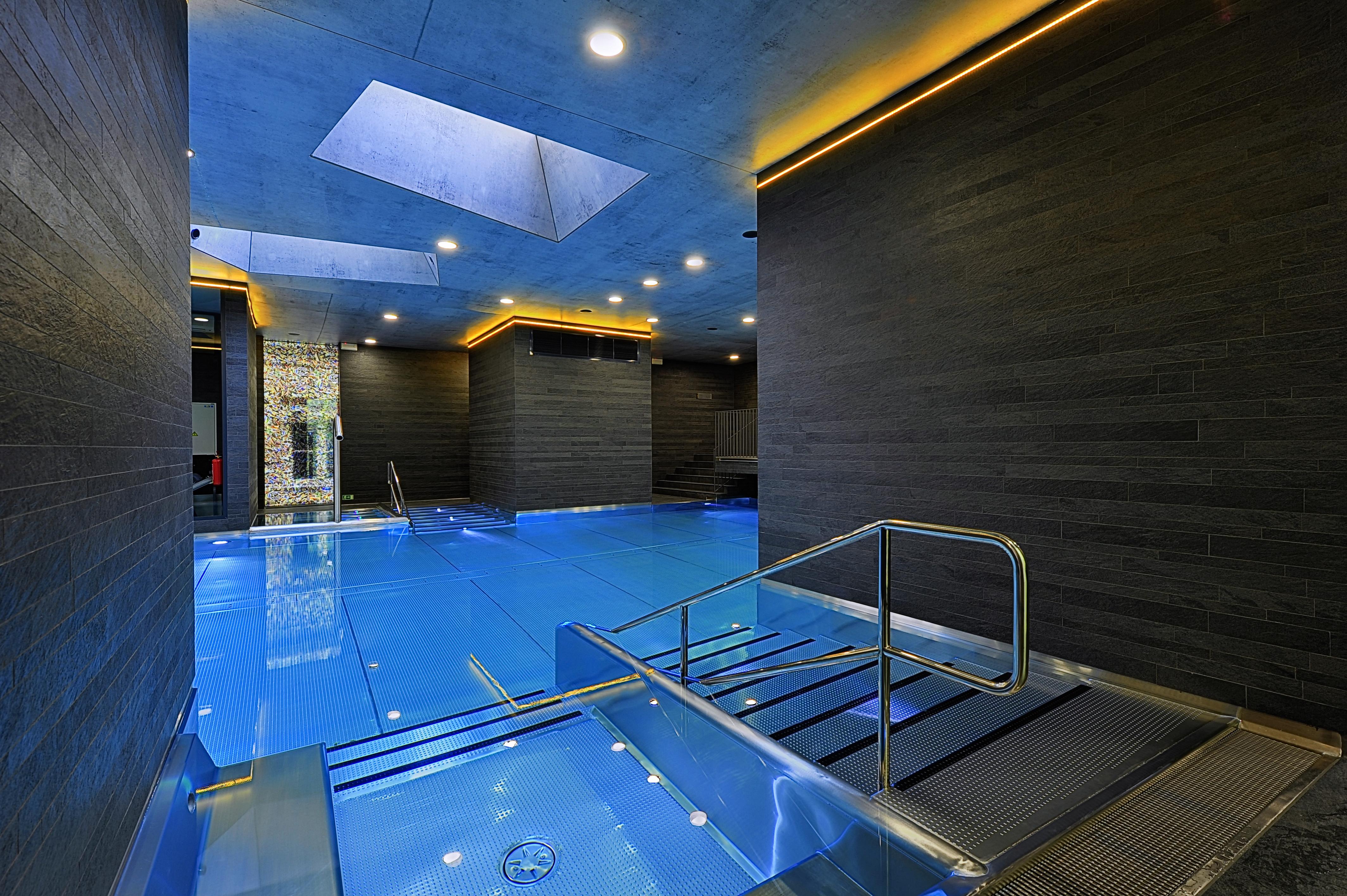 Grandhotel Pupp Karlovy Vary Ngoại thất bức ảnh The photo features a modern indoor swimming pool area. The pool is designed with a sleek, contemporary aesthetic, featuring a vibrant blue water surface. The surrounding walls are made of dark materials, possibly stone or wood, complemented by warm l
