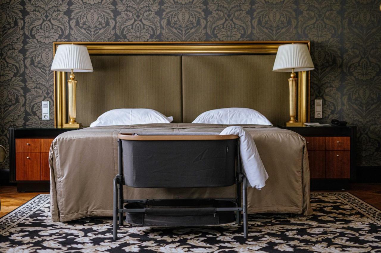 Grandhotel Pupp Karlovy Vary Ngoại thất bức ảnh The photo shows a cozy hotel room with a stylish design. In the center, there are two beds with white pillows and a beige bedspread. Flanking the beds are two elegant lamps on side tables, and behind the beds is a large gold-framed headboard. At the 