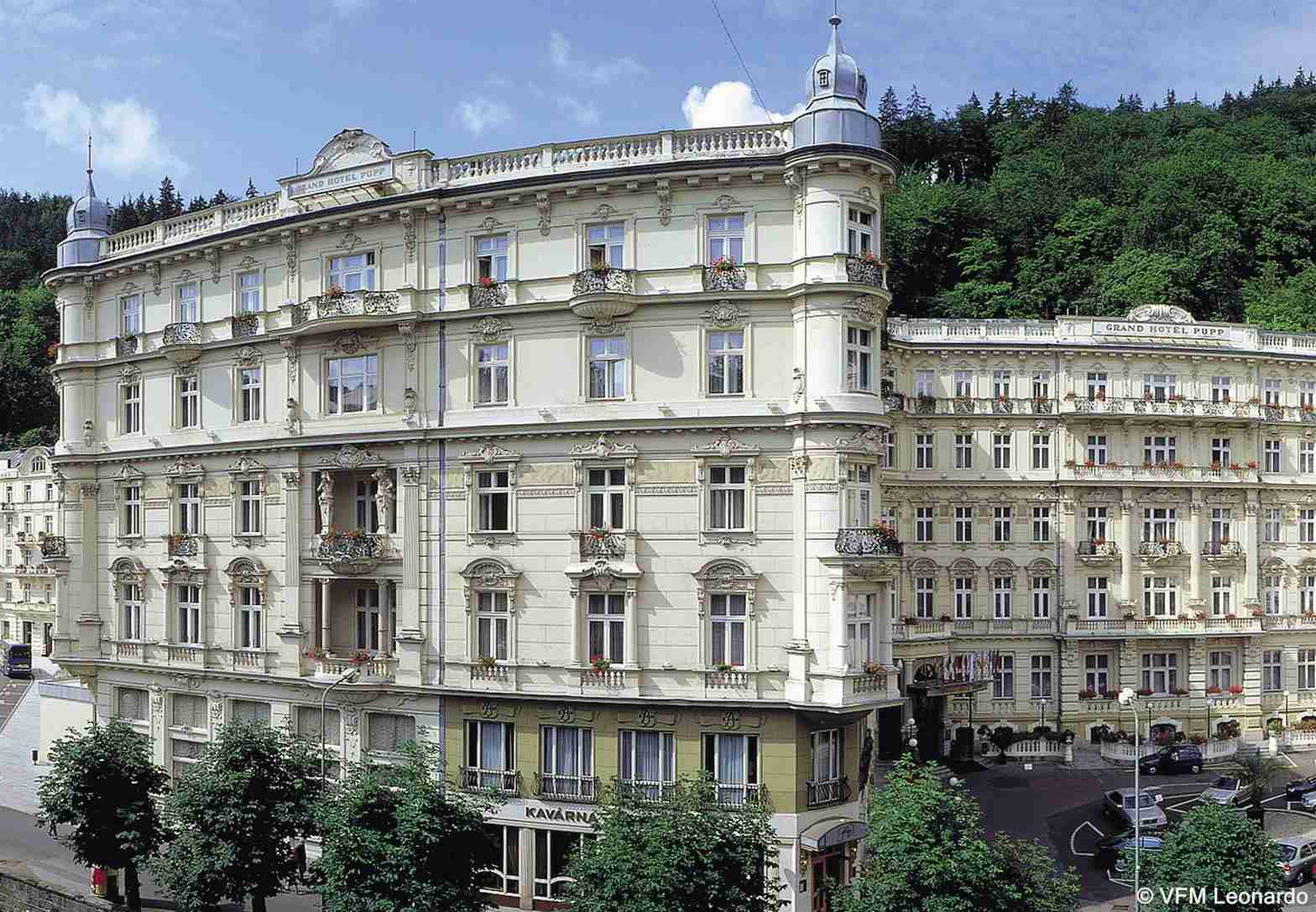Grandhotel Pupp Karlovy Vary Ngoại thất bức ảnh The photo shows a beautiful architectural scene featuring two elegant buildings. The structures exhibit a classic design with intricate details, large windows, and ornate balconies. They are painted in a light color, possibly cream or pale yellow, wh